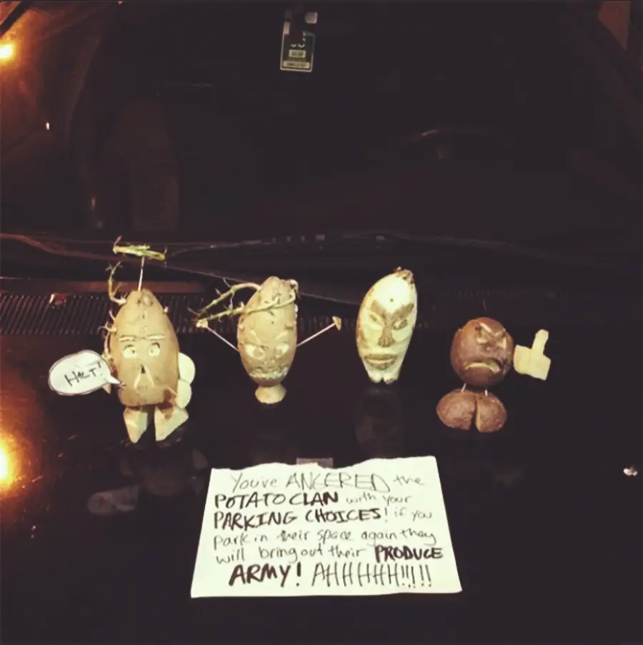 Five decorated potatoes with faces and arms are lined up on a car hood. A handwritten note warns about angering the "Potato Clan" for poor parking choices, threatening a "produce army" if it happens again.