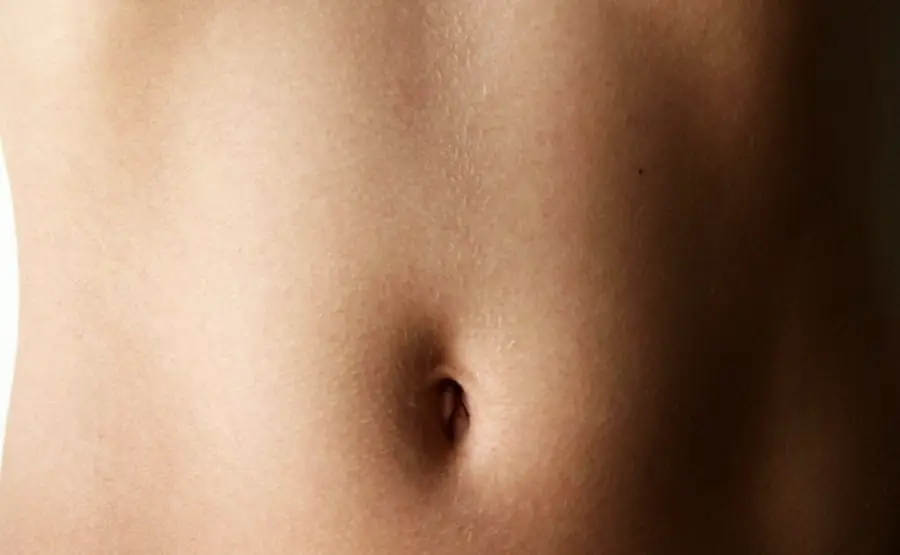 Close-up of a person's bare midsection focusing on the navel, with smooth, light-toned skin and soft lighting.