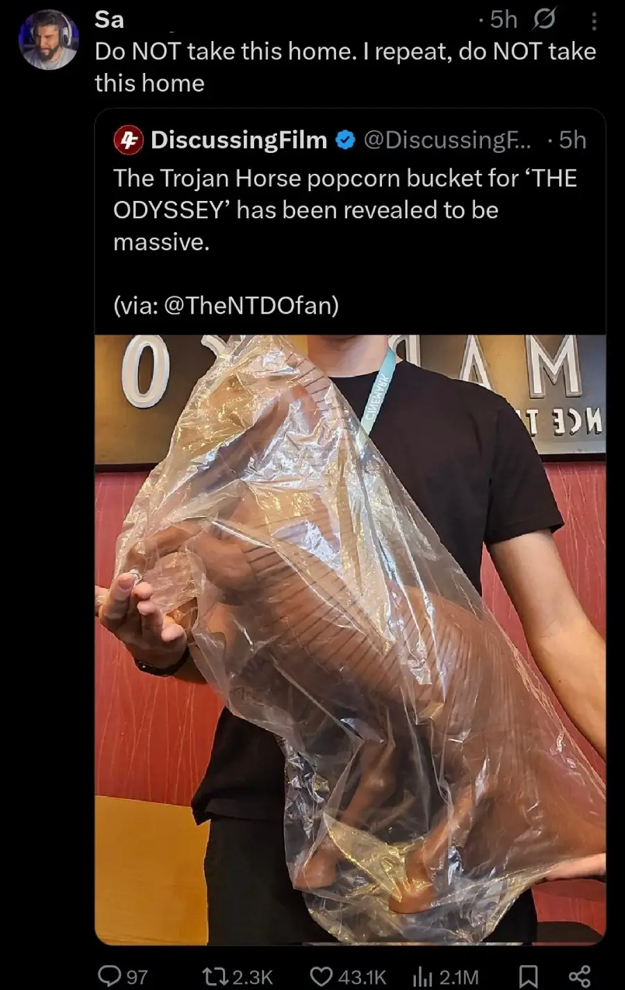 A person holds a large, detailed Trojan Horse popcorn bucket wrapped in clear plastic; a tweet above warns, "Do NOT take this home. I repeat, do NOT take this home.