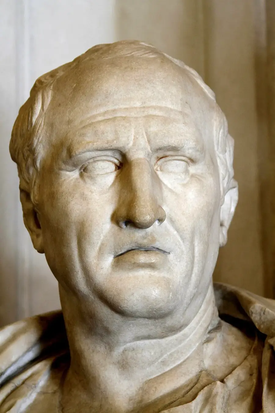Marble bust of an older man with short hair and a serious expression, wearing a draped garment. The sculpture shows realistic facial details, including wrinkles and a prominent nose. Background is plain and neutral.