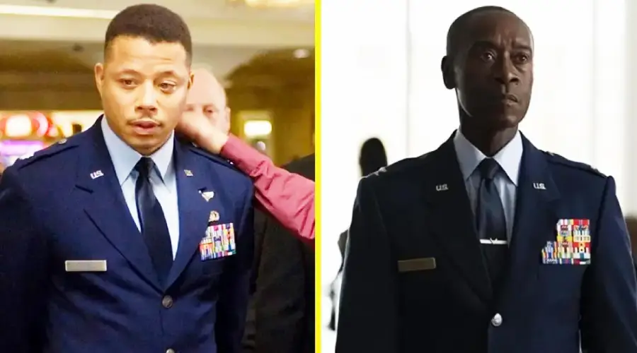 Two men wearing dark blue military uniforms with badges and ties; the man on the left is being touched on the shoulder, while the man on the right stands alone in a bright setting.