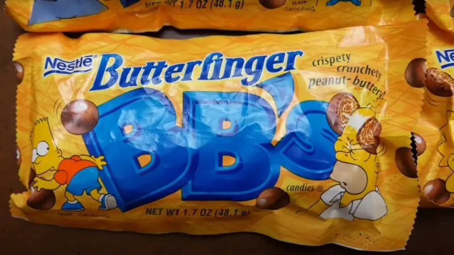 A yellow Butterfinger BB's candy bag featuring cartoon characters Bart Simpson kicking the logo and Homer Simpson eating candy. The packaging highlights "crispy, crunchy, peanut-buttery" treats.