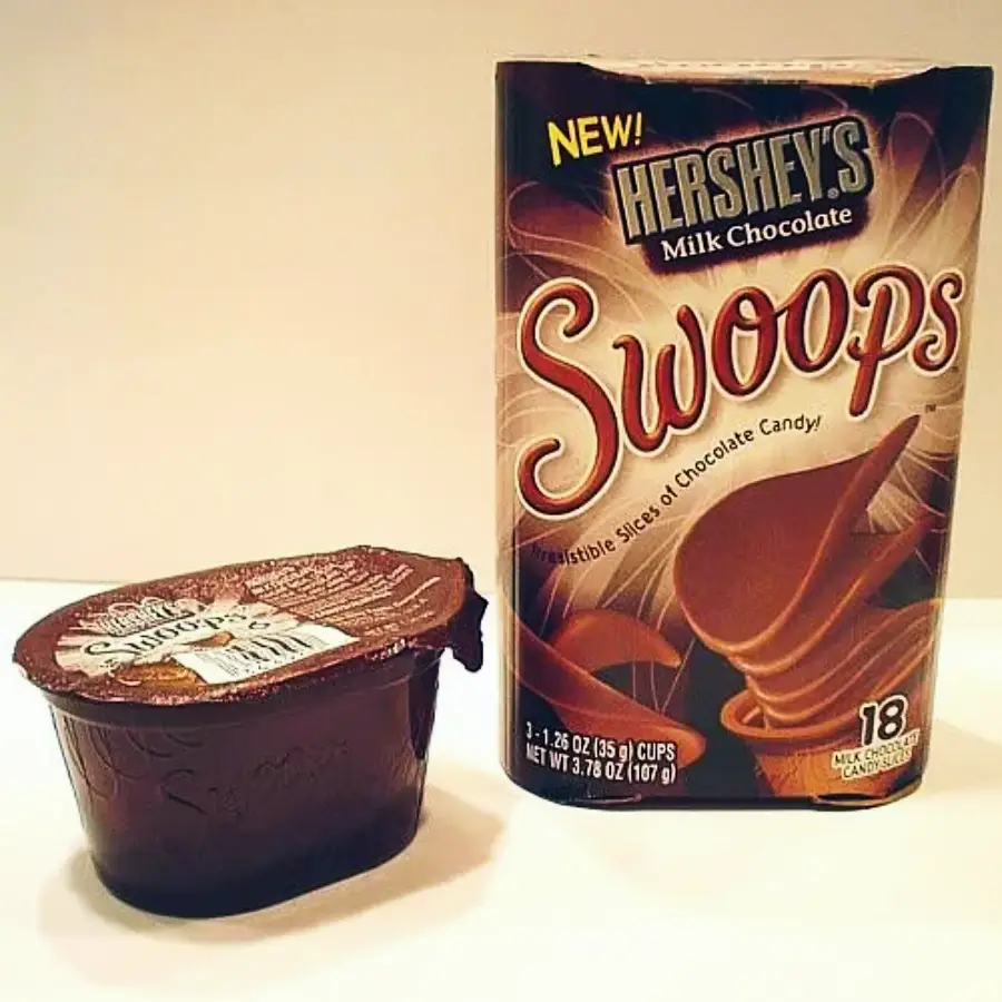 A container of chocolate pudding sits next to a Hershey's Milk Chocolate Swoops box, which shows curved chocolate slices on the packaging.
