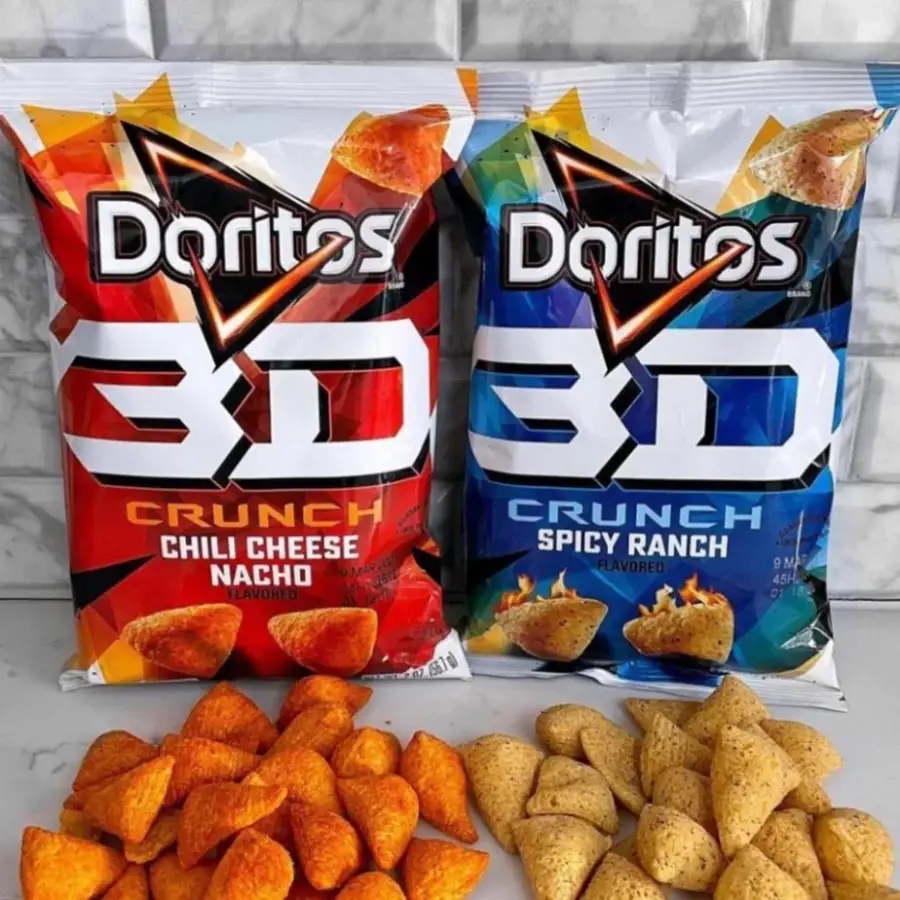 Two bags of Doritos 3D Crunch chips, one Chili Cheese Nacho (red bag) and one Spicy Ranch (blue bag), with piles of each flavor’s puffed triangular chips arranged in front of the matching bags.