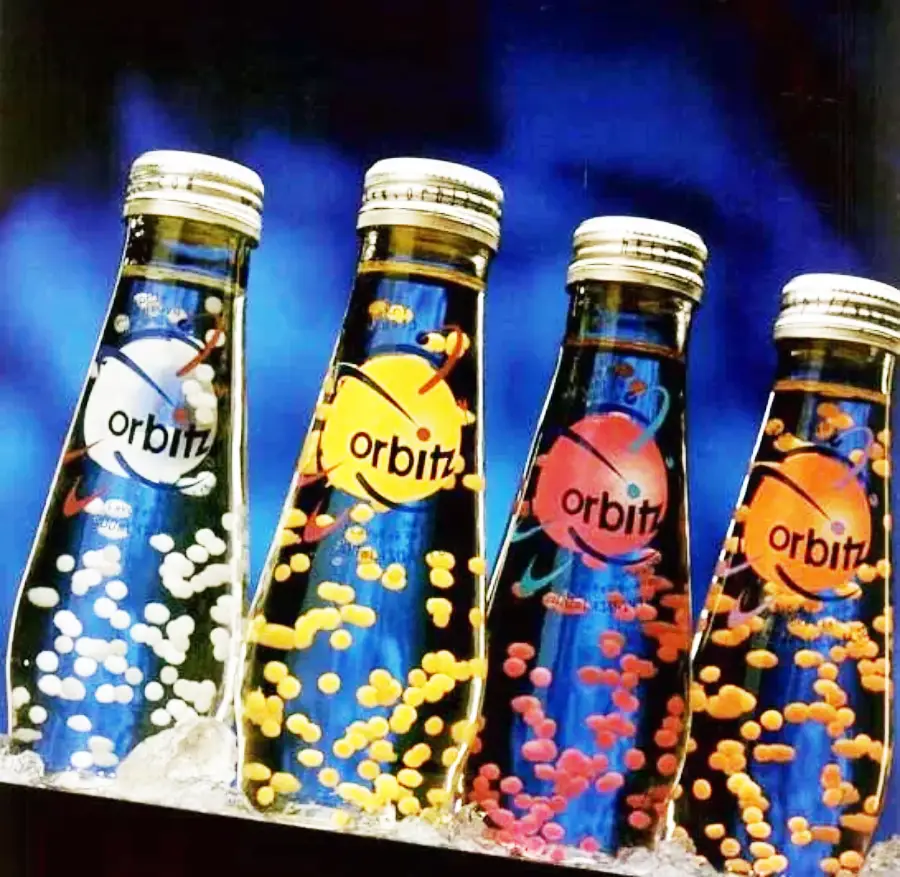Four glass bottles of Orbitz drink are shown side by side, each filled with floating colored spheres. The bottles have different labels and colors, set against a blue background.