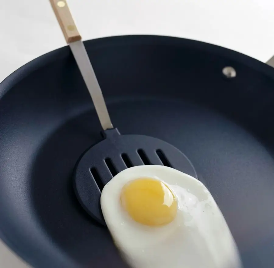 A cooked sunny-side-up egg is being lifted from a black nonstick frying pan with a spatula.