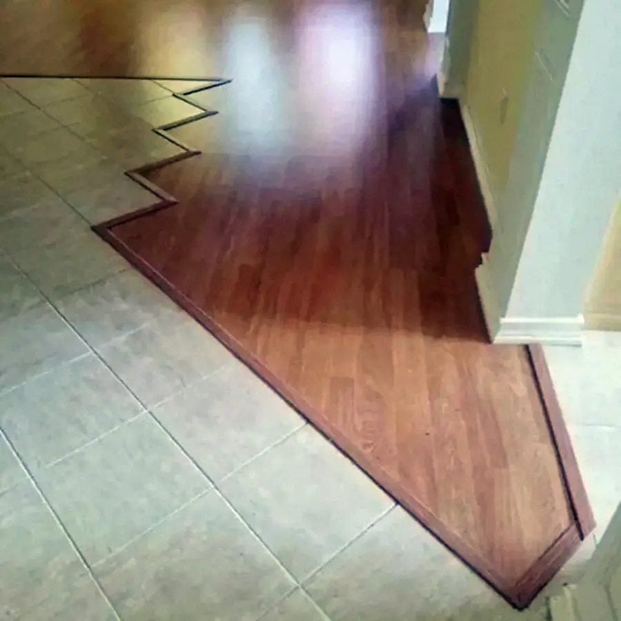 A floor with a jagged zigzag transition between beige tiles and brown wood flooring, creating an unusual geometric border between the two surfaces.