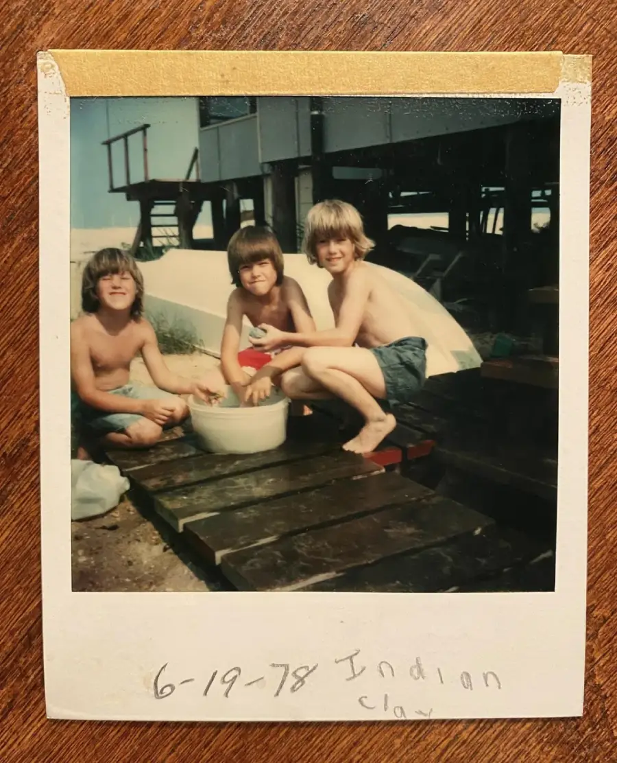 Three children in swimsuits sit on a wooden deck outside near a large bowl of water, smiling at the camera. The photo appears old, dated "6-19-78 Indian clay," with beach houses in the background.