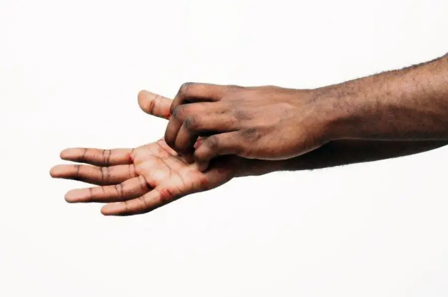 A person using their right hand to scratch the palm of their left hand against a plain white background.