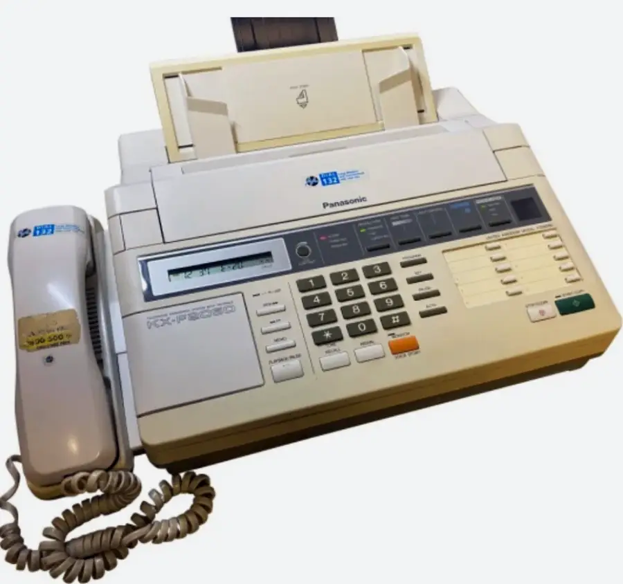 A vintage Panasonic fax machine with a built-in telephone handset, numeric keypad, function buttons, display screen, and paper feeder on top. The device is off-white in color and has a coiled phone cord.