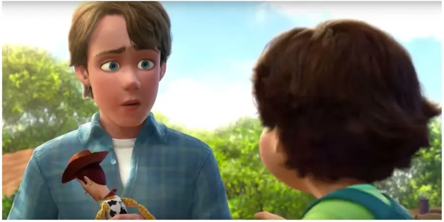 A teenage boy in a blue plaid shirt holds a cowboy doll and looks at a young child with brown hair, who is facing him. They are outdoors with trees and sunlight in the background.