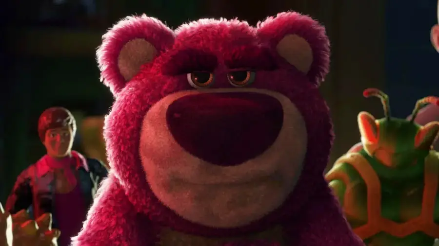 A large, pink, fuzzy bear with a stern expression stands in the center, with a toy soldier and a green insect-like character in the background, all illuminated by dramatic lighting.
