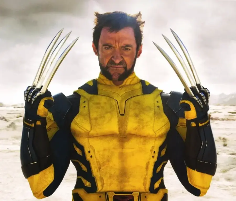 A man in a yellow and black superhero costume stands outdoors with metal claws extended from his hands, looking serious and intense.
