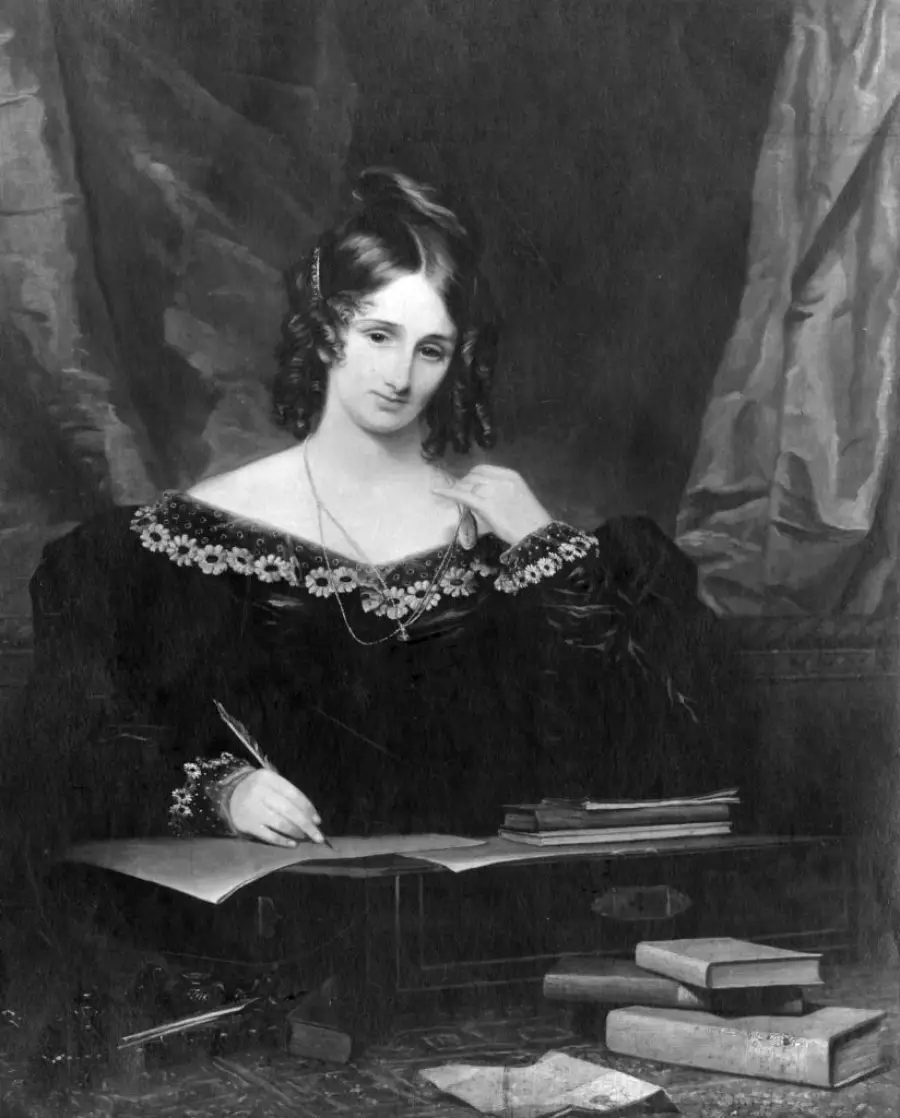 A woman in a dark dress sits at a desk, writing on paper with a quill pen. Several books and papers are on the desk. She looks thoughtfully at the viewer, with a curtain backdrop behind her.
