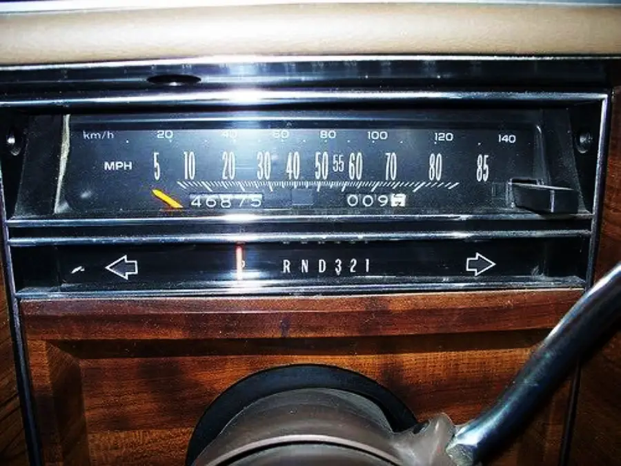 Close-up of a vintage car dashboard showing a speedometer with a maximum of 85 mph, odometer reading 46875 miles, and gear shift indicator on a woodgrain panel.