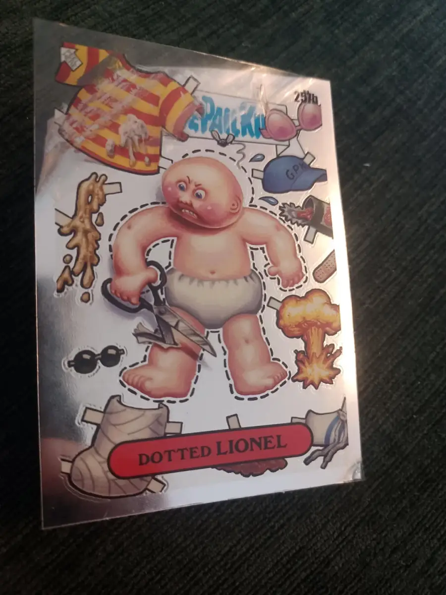A sticker card labeled "Dotted Lionel" shows a cartoon baby with scissors, surrounded by cutout clothes, objects, and quirky items on a dark textured surface.