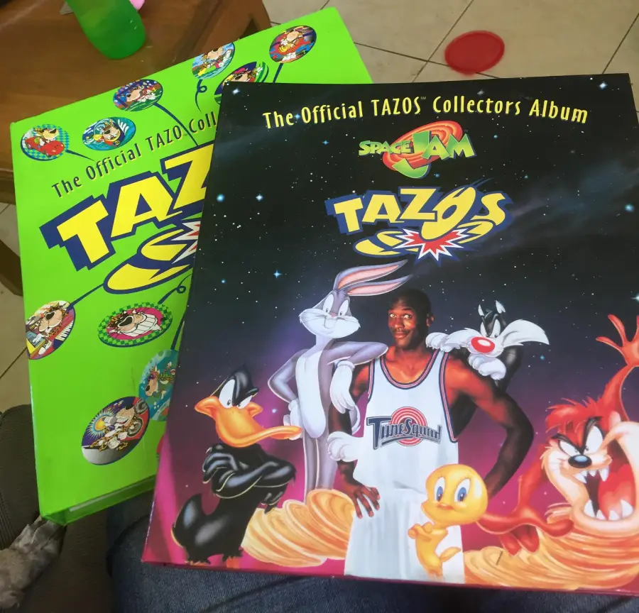 Two TAZOS collector albums are shown, one bright green with cartoon characters, and one featuring Space Jam with Looney Tunes characters and a basketball player on the cover.
