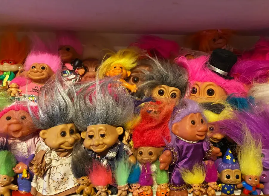 A colorful collection of troll dolls with wild, bright hair and various outfits crowded together on a shelf.