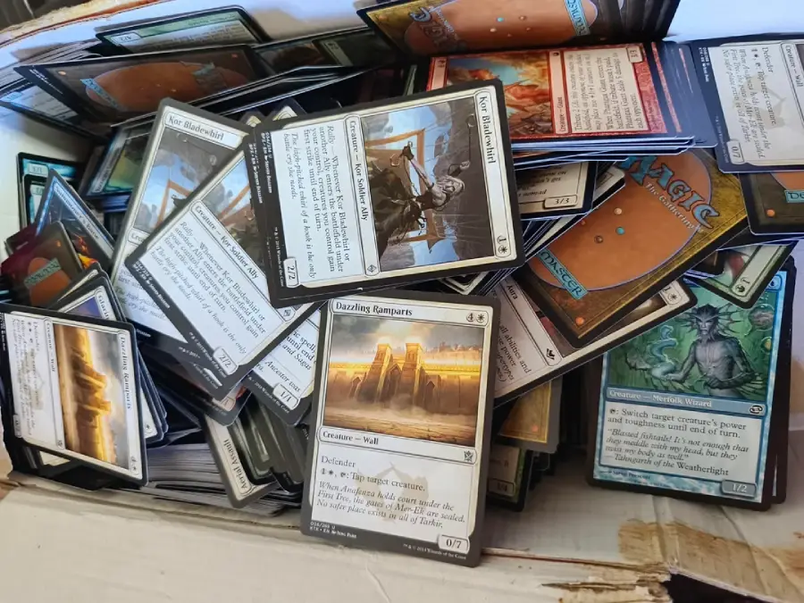 A large pile of assorted Magic: The Gathering cards in a white box, featuring various colors, card types, and artwork, some cards facing up and others scattered in different directions.