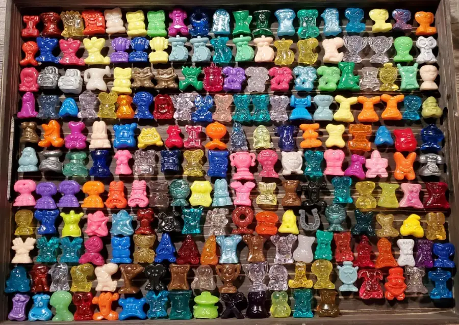 A collection of colorful, small plastic figurines neatly arranged in a grid, each with distinct shapes and colors, filling a rectangular tray.