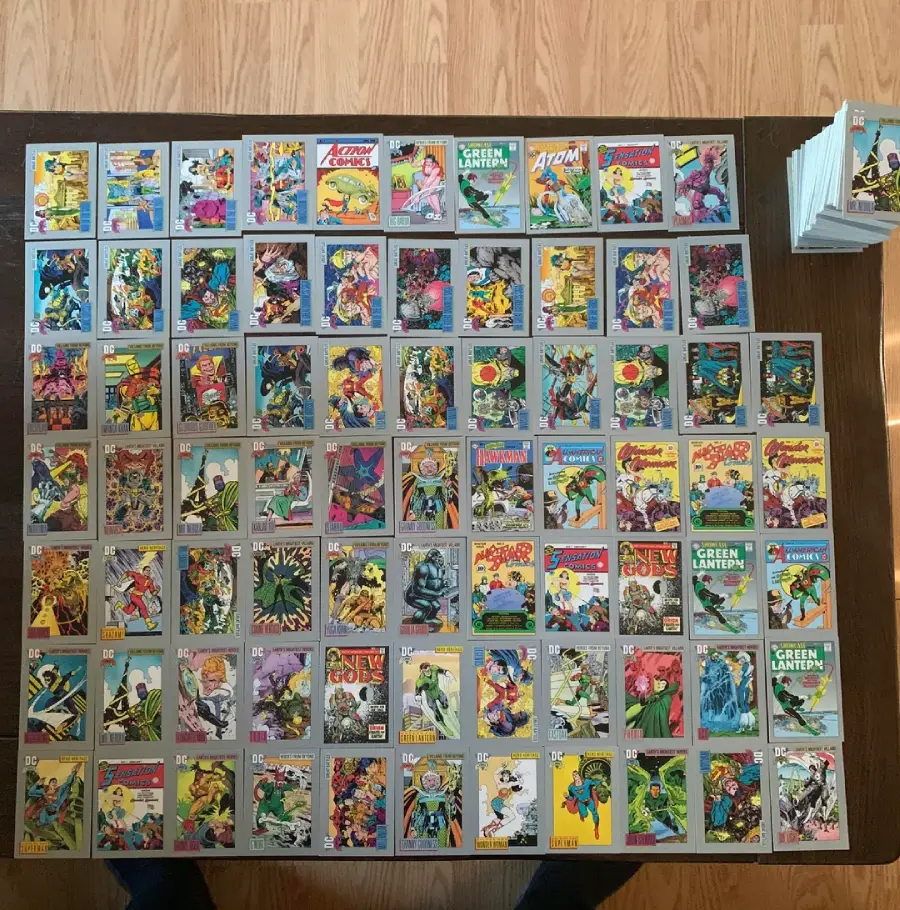 A collection of vintage comic books arranged neatly in rows on a wooden table, with a small stack in the top right corner. The covers are colorful and feature various superheroes in dynamic poses.