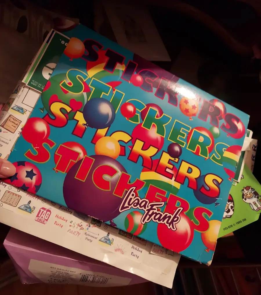 A Lisa Frank sticker sheet with colorful "STICKERS" text, stars, and balloons, placed on a pile of papers and envelopes.