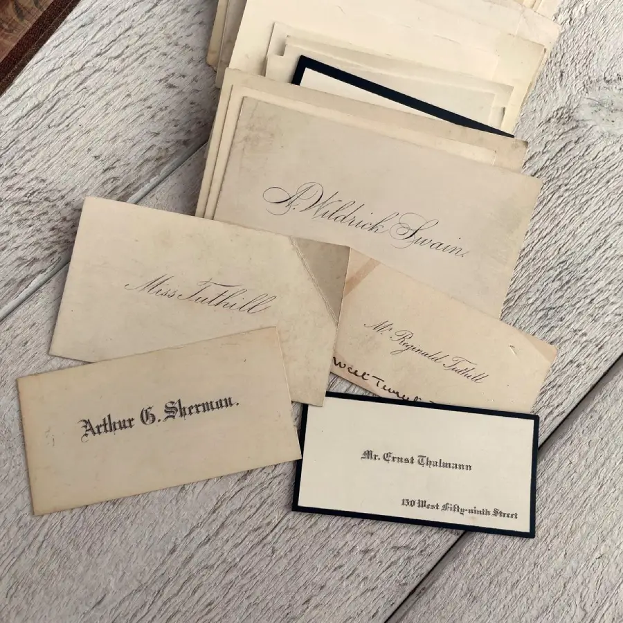 A stack of vintage calling cards with elegant script, featuring names like Arthur G. Sherman, Mr. Ernest Thalman, and Miss Tatchell, displayed on a light wooden surface.