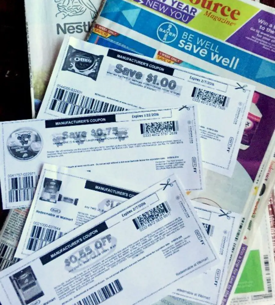 Several manufacturer’s coupons offering discounts are spread out on top of a stack of magazines and flyers, including one with an Oreo cookie image and the words “Save $1.00.”