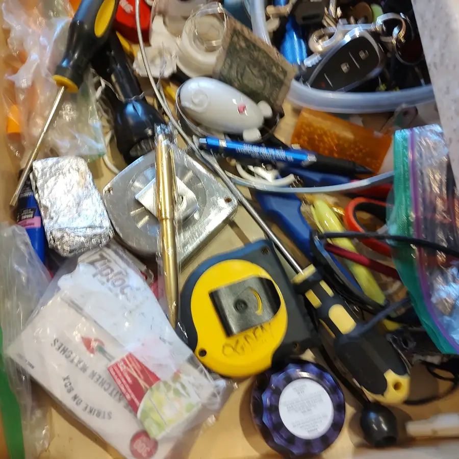 A cluttered drawer filled with a tape measure, screwdriver, pen, key fobs, small tools, plastic bags, and assorted everyday items.