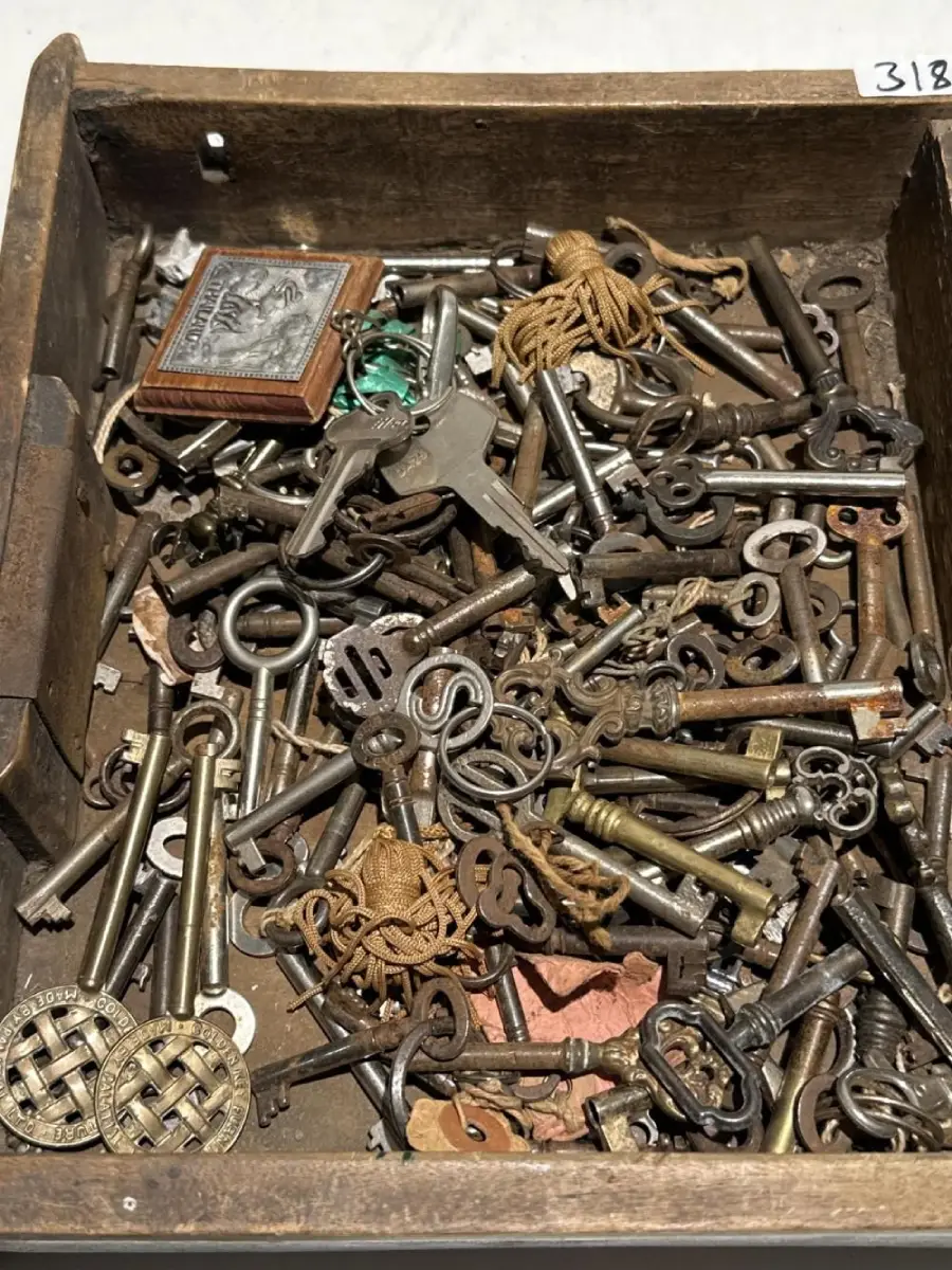 A wooden drawer filled with assorted vintage keys, keychains, tangled string, a small framed photo, and metal trinkets in various shapes and sizes.