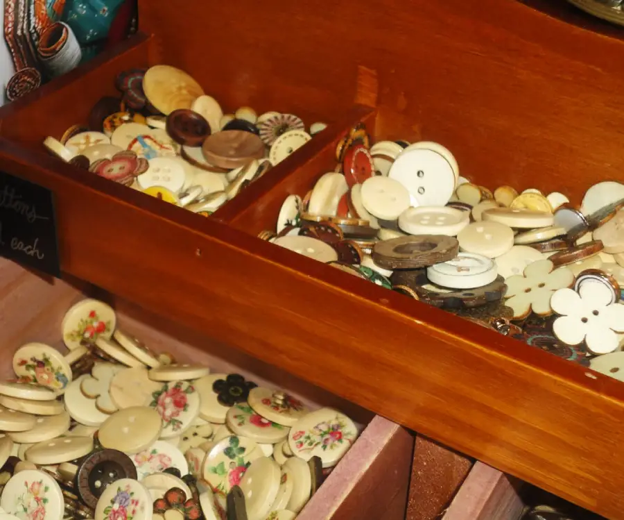 Wooden drawers filled with an assortment of vintage buttons, some with floral designs and others plain. The buttons vary in shape, color, and size, creating a colorful, nostalgic display.