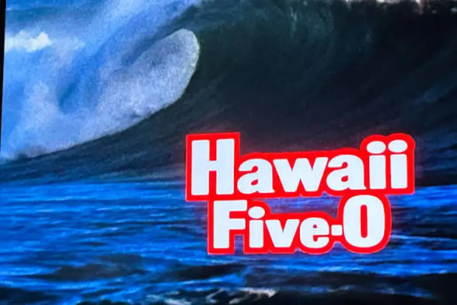A large ocean wave with the text "Hawaii Five-O" in bold white and red letters overlaying the water.