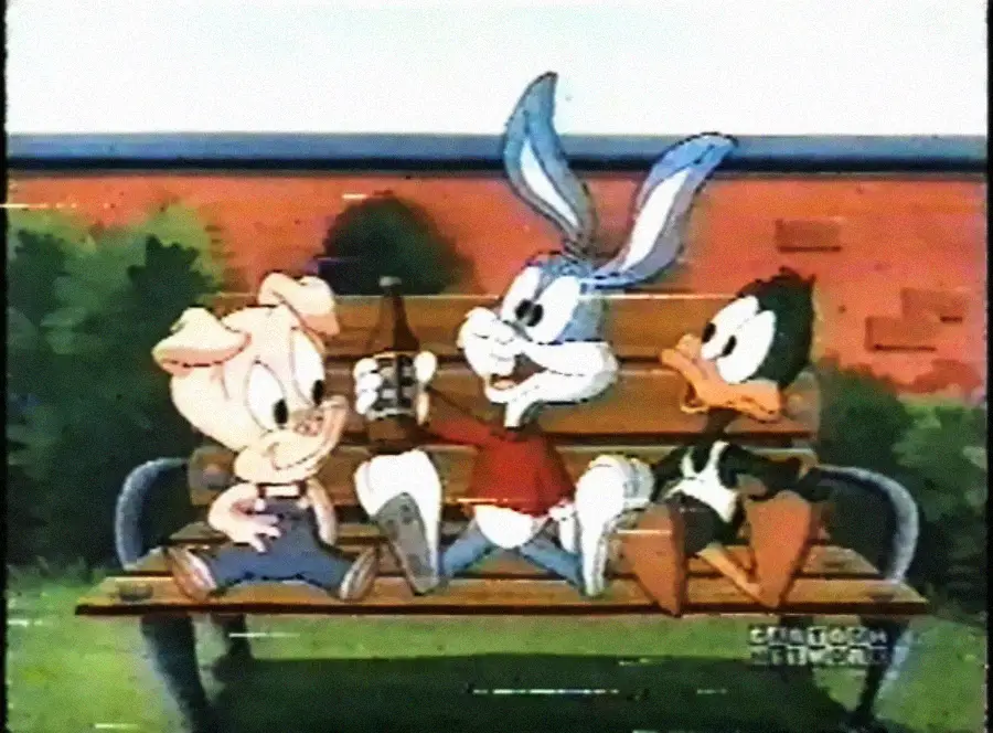 Three cartoon characters—a pig, a gray rabbit, and a black duck—sit together on a park bench. The rabbit holds a drink and is smiling at the pig, while the duck looks on. Trees and a red wall are in the background.