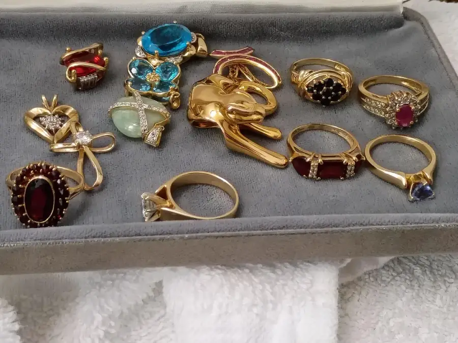 A display of gold rings with various gemstones and designs, arranged on a gray jewelry tray with a white towel underneath.