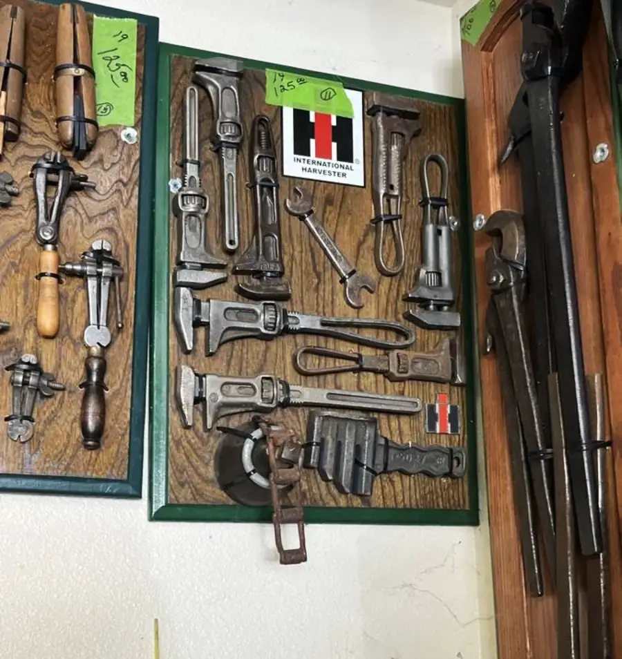 A display of vintage wrenches and hand tools mounted on a wooden board with International Harvester logos and price tags, hung on a wall.