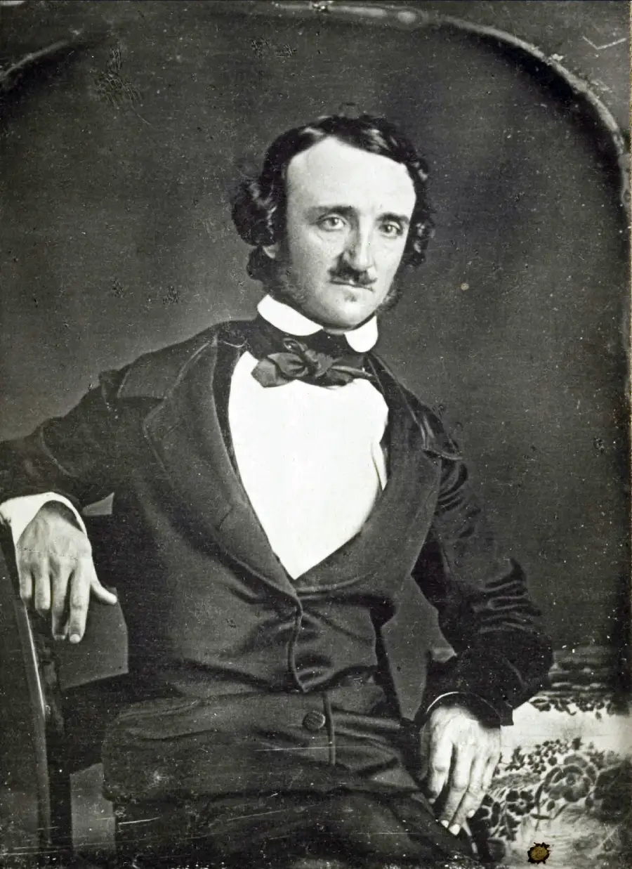A man in a dark suit with a bow tie sits, gazing forward with one arm resting on a table. The black-and-white portrait has a vintage, 19th-century style.