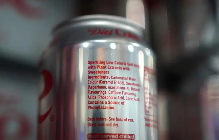 A close-up of a silver soda can shows the ingredients and nutritional information in red text, with the background and parts of the can blurred.