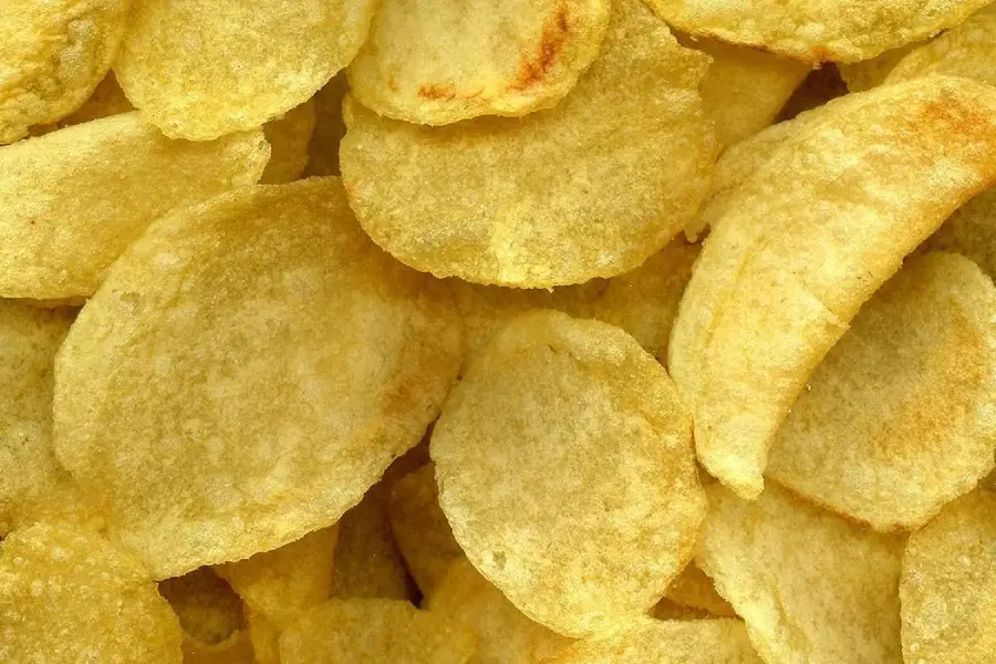 Close-up view of a pile of golden, crispy potato chips, showing their round, wavy texture and light seasoning.