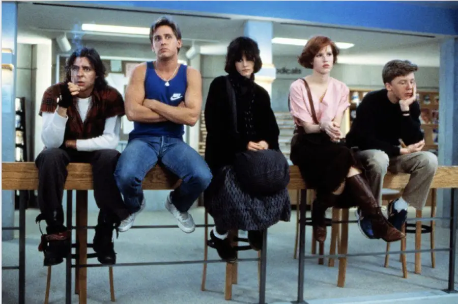 Five teenagers sit on a table in a school library, each dressed differently, with varied expressions, suggesting distinct personalities.