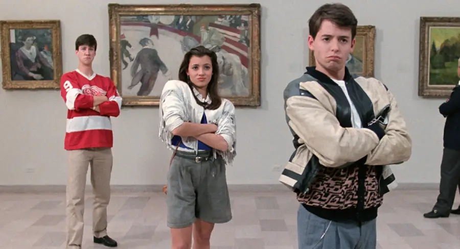 Three teenagers stand with arms crossed in an art gallery, paintings on the wall behind them. The boy in front wears a patterned jacket, the girl in the middle wears a white jacket, and the boy in back wears a red hockey jersey.