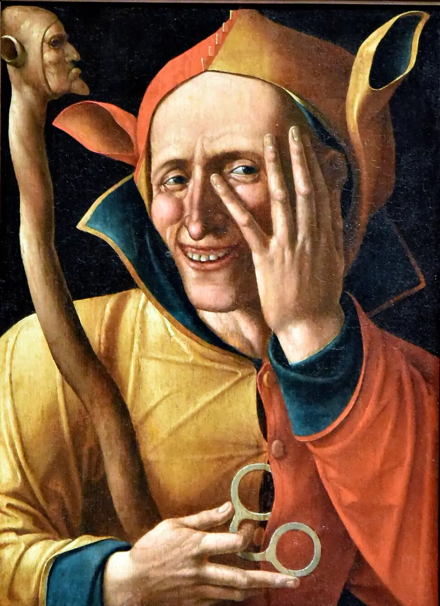 A medieval jester in colorful attire smiles mischievously, holding a staff topped with a carved head and wearing a cap with ear-like points. One hand partially covers his face, revealing a playful expression.
