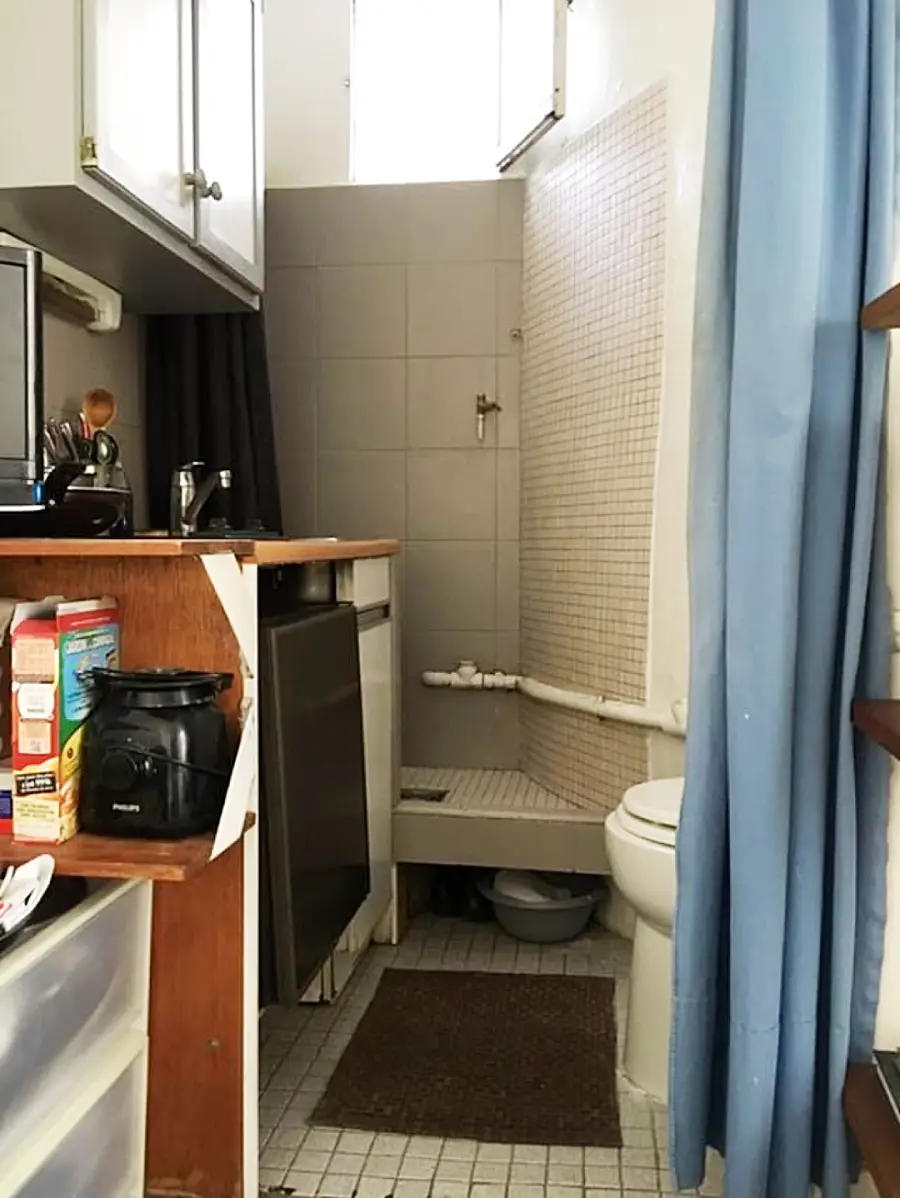 Small kitchen and bathroom combined in one space, with a counter, sink, cereal boxes, toilet, shower, and blue curtain. Minimal floor space and overhead cabinets are visible.