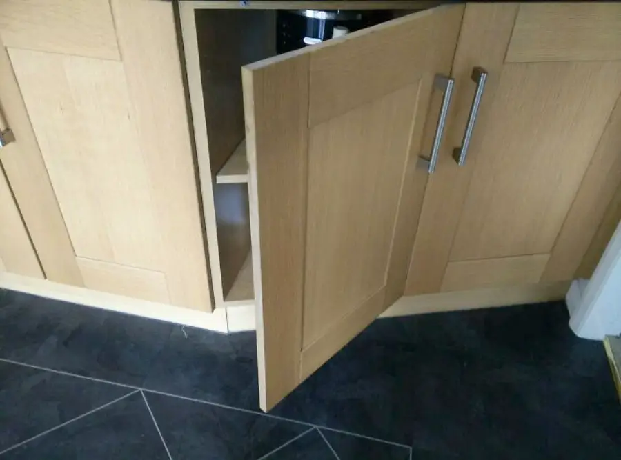 A kitchen cabinet with two doors is shown. One door is open, but its hinges are installed on the wrong side, causing it to block the other door.