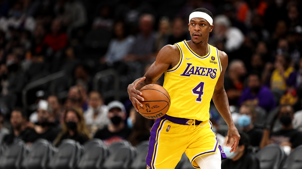 A basketball player in a yellow Lakers uniform dribbles the ball on court during a game, with spectators visible in the background.