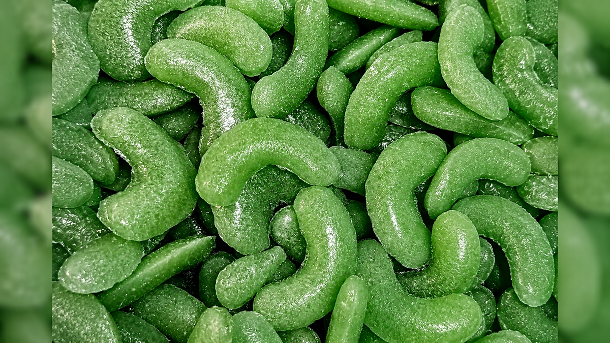 Close-up of many green, curved, sugar-coated gummy candies tightly packed together, resembling small caterpillars or crescent shapes.