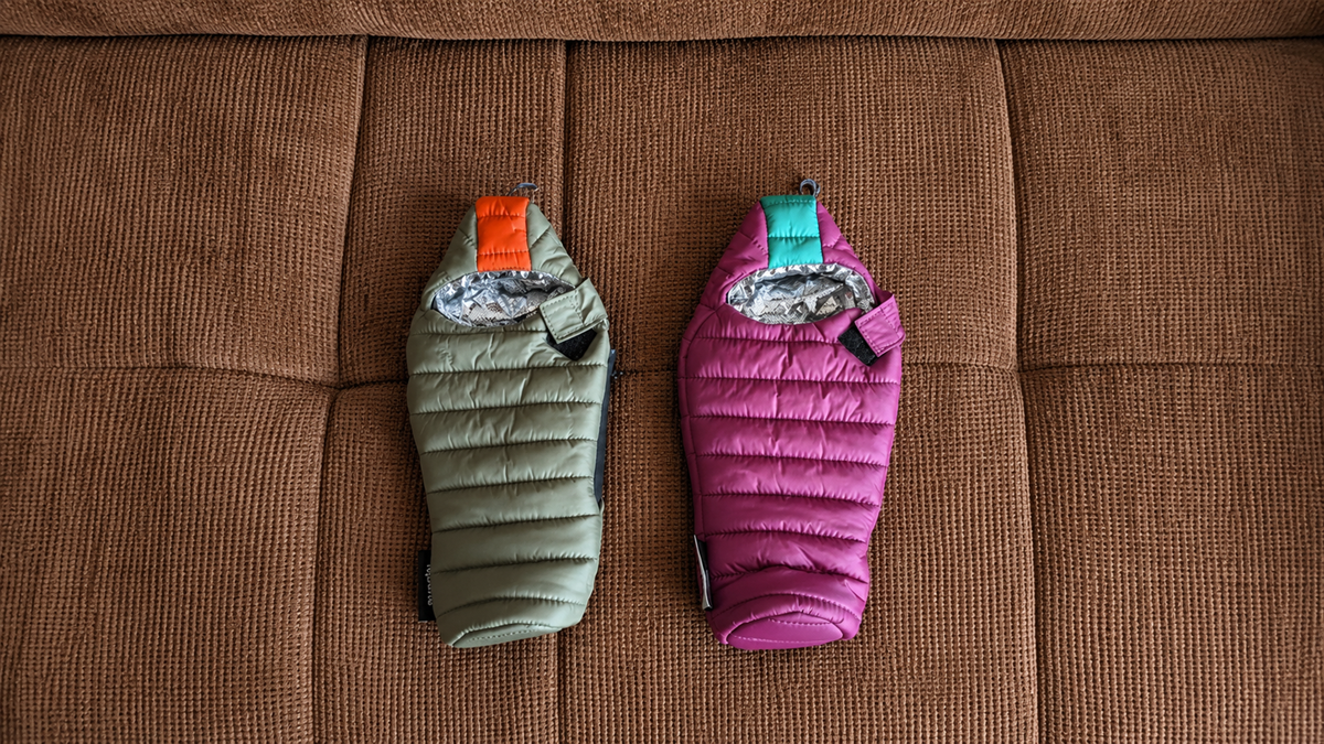 Two insulated bottle covers, one green with an orange tag and one purple with a turquoise tag, are placed side by side on a textured brown surface.