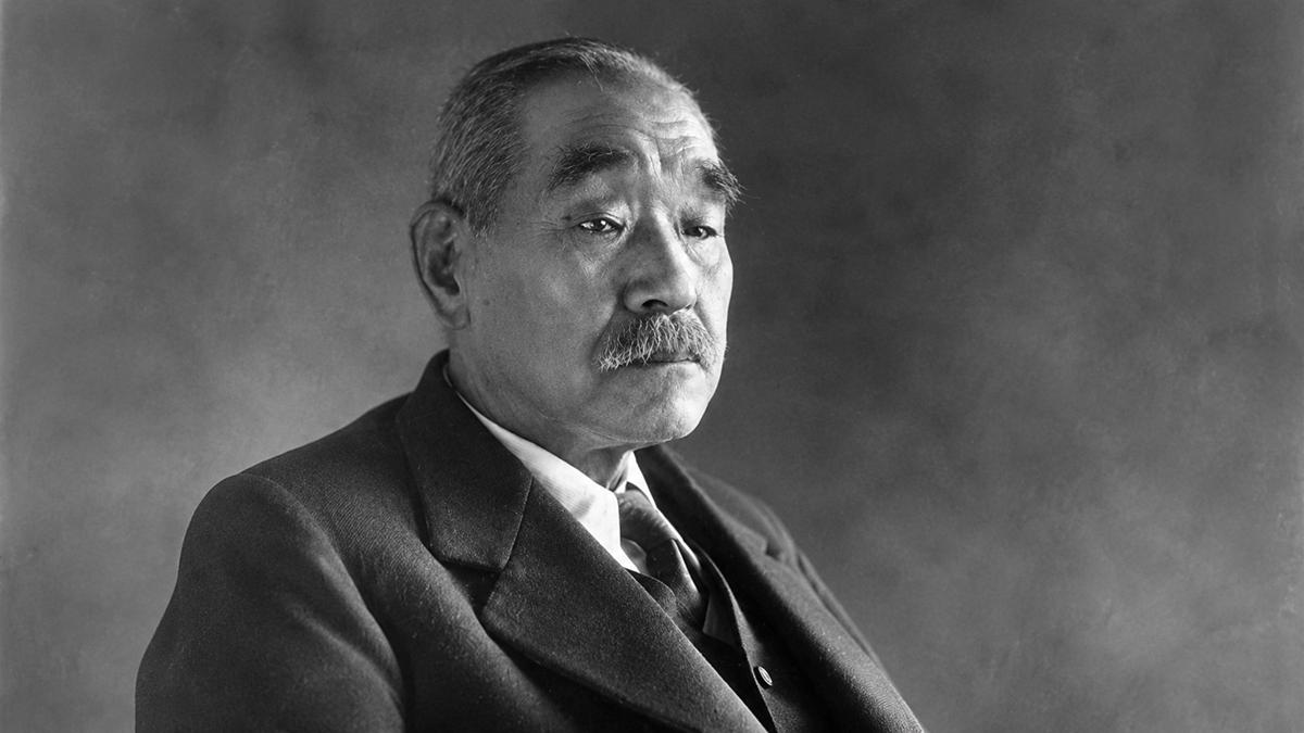 An elderly man with short hair and a mustache, wearing a suit and tie, poses for a formal black-and-white portrait against a plain background.