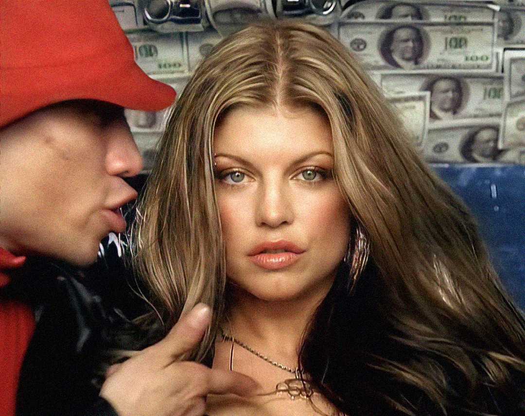 A woman with long, wavy brown hair wearing hoop earrings and a necklace stands in front of a wall covered with U.S. dollar bills. A person in a red hat and jacket gestures near her.