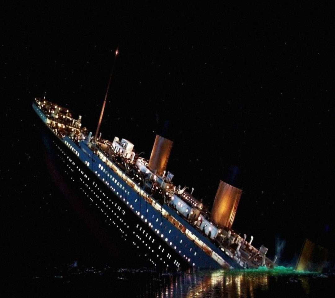A large ship with lit windows and three smokestacks tilts steeply in dark water at night, with smoke and lights indicating distress. The sky is black, suggesting a disaster at sea.