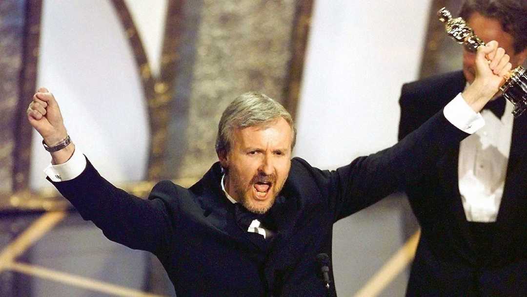 A man in a tuxedo celebrates on stage, raising an Oscar trophy in one hand and clenching his other fist, with a jubilant expression at an awards ceremony.